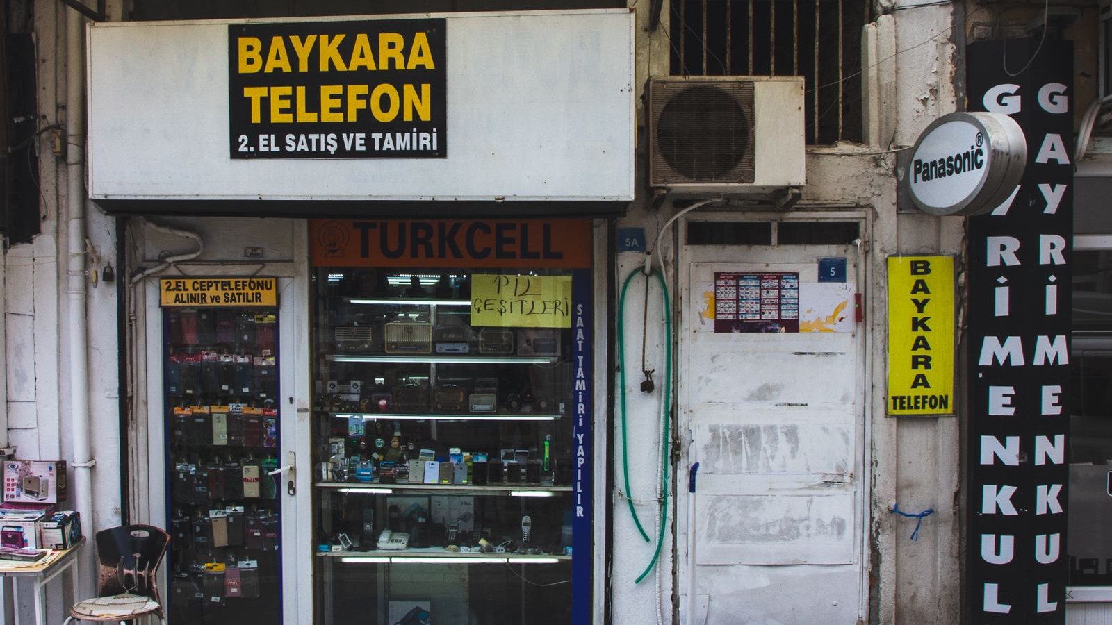 Sokaktan görünen bir cep telefonu dükkânı; tabelada firma adı ve yapılan iş büyük harflerle yazılı.